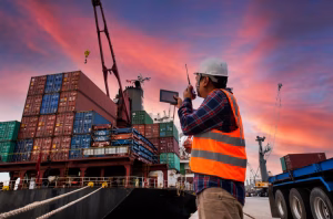 Port logistics officer coordinating container unloading at a shipping dock during sunset